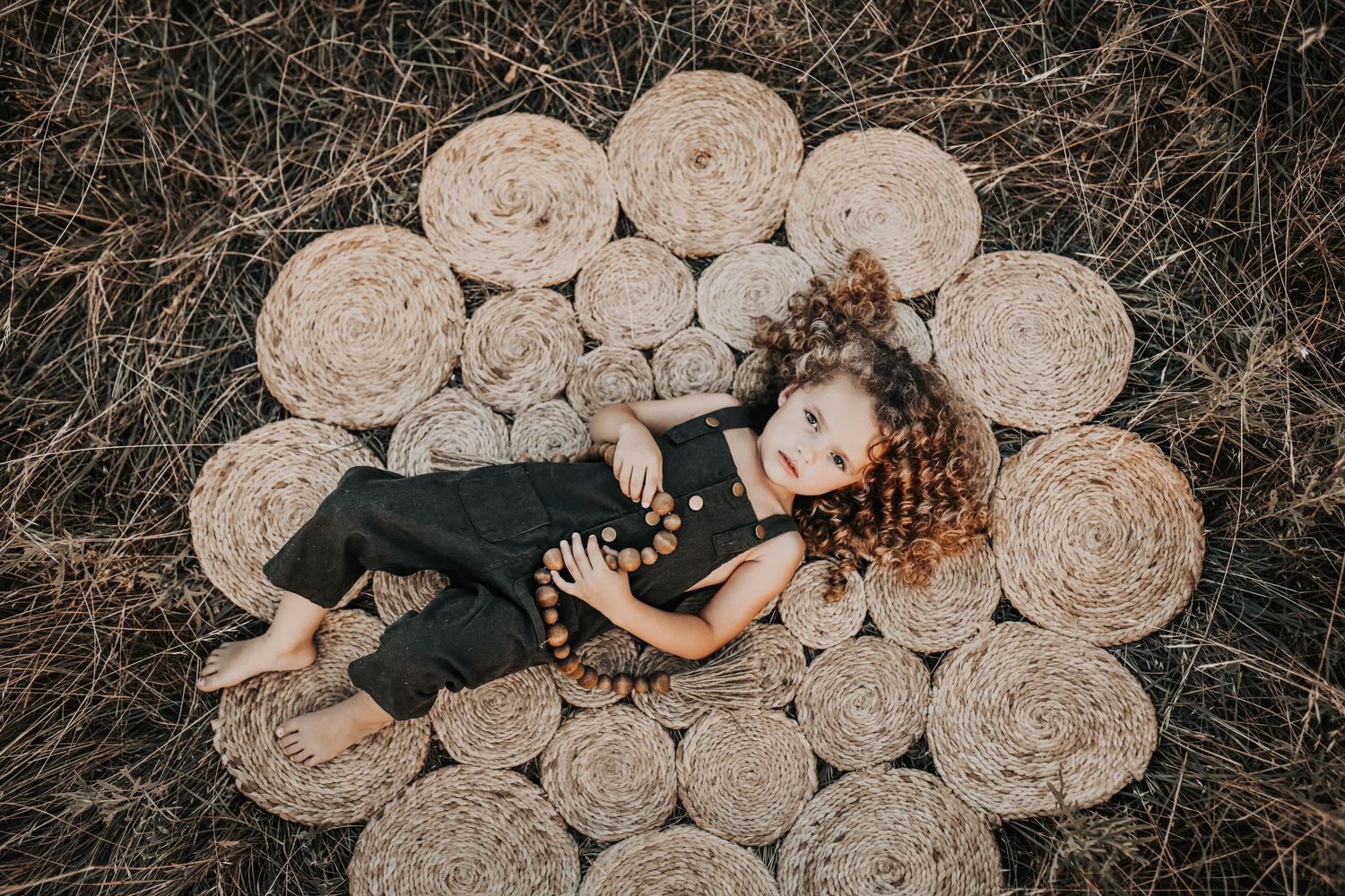 a curly haired little girls lays on her back on a boho rug in a field at sunset for family photos at murrell park in grapevine