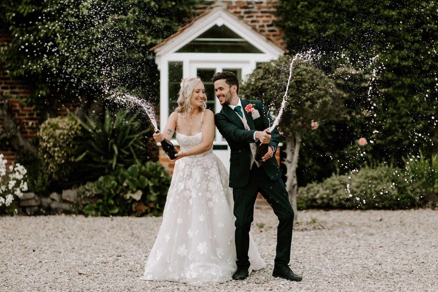 A couple celebrates their wedding day with sparklers outside a brick building with white columns and lush landscaping.