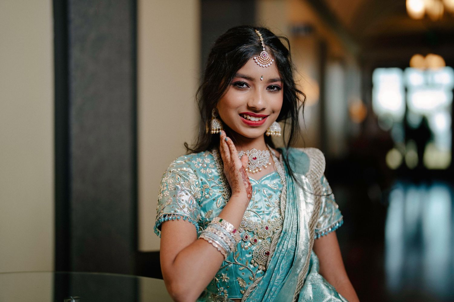 Traditional South Asian bride in mint green sari and silver jewelry poses elegantly in soft indoor lighting.