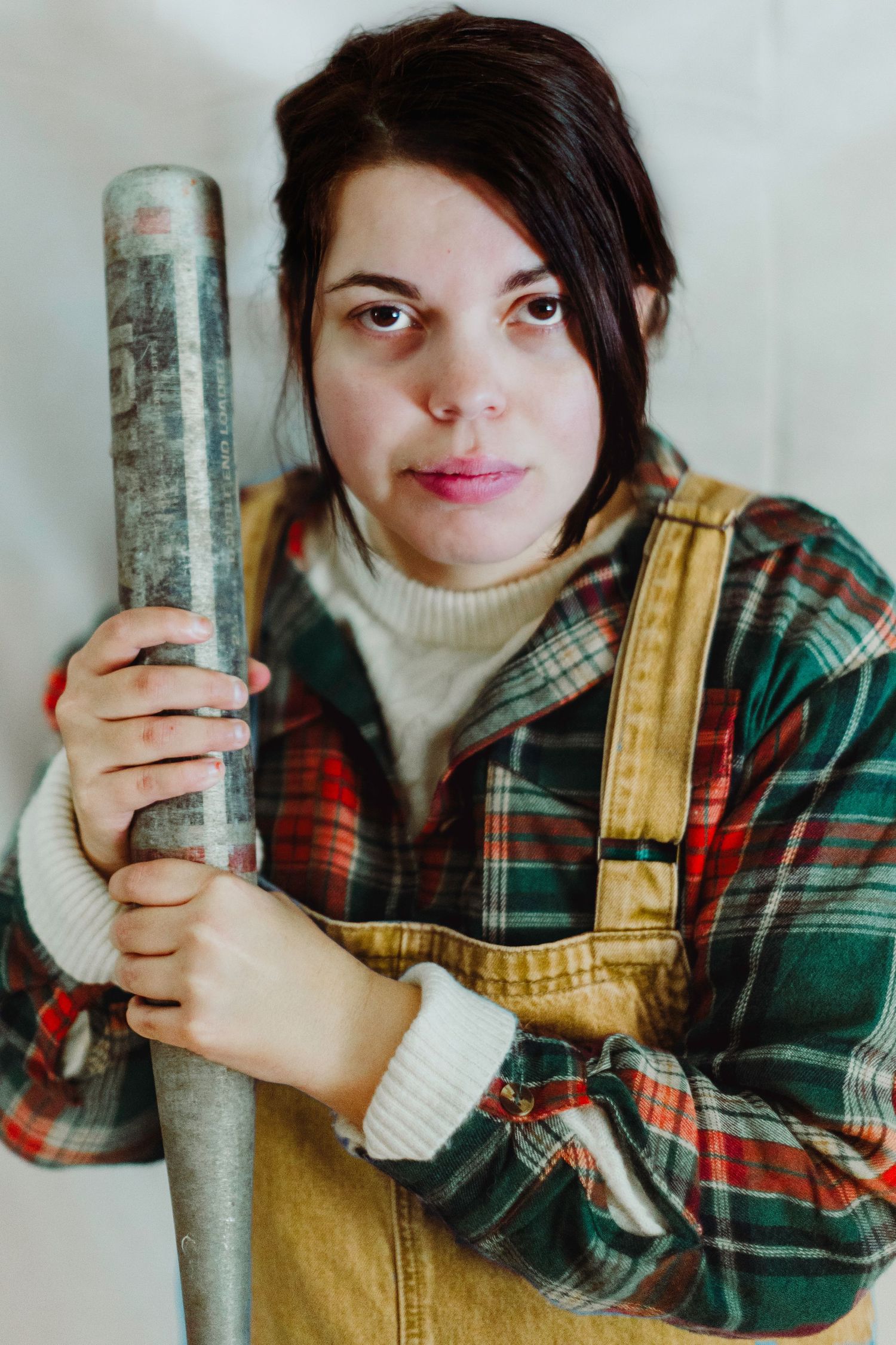 A person in a plaid flannel shirt and overalls poses playfully with a metal pipe in a series of four photos.