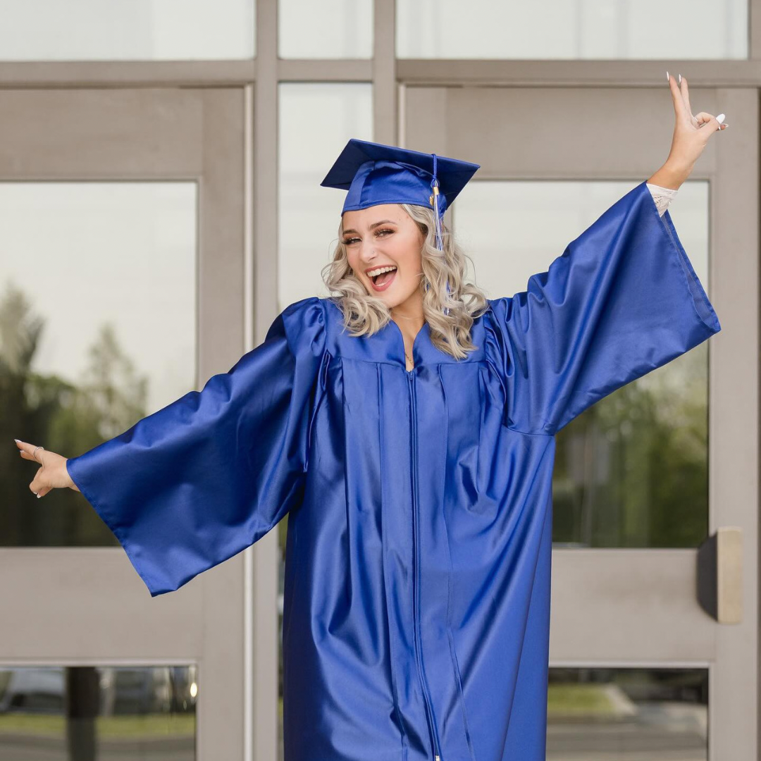 Graduate in royal blue cap and gown poses joyfully against white background.