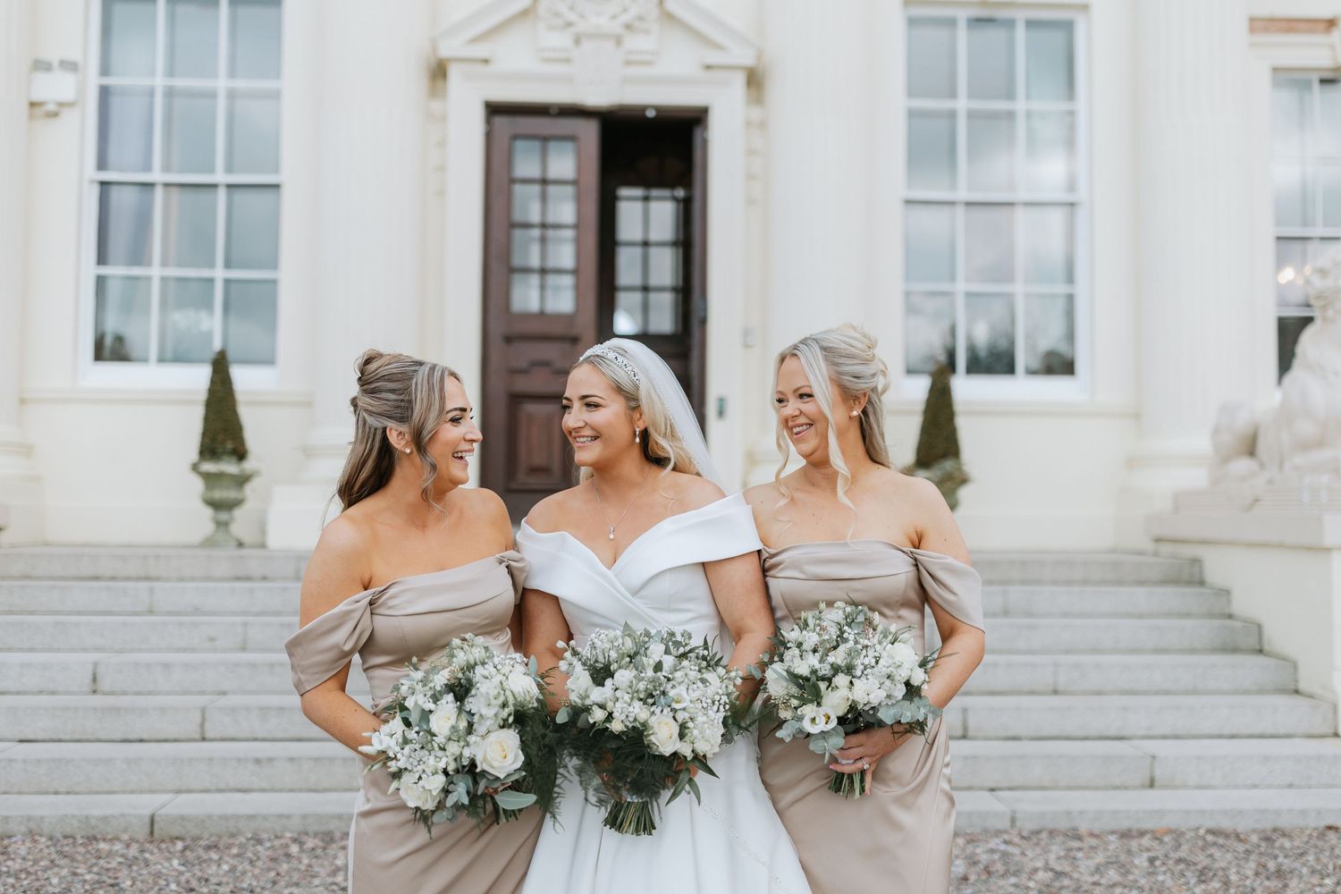 A romantic wedding couple shares a tender moment on a path leading to a grand historic mansion with red brick details. Hawkstone Hall.