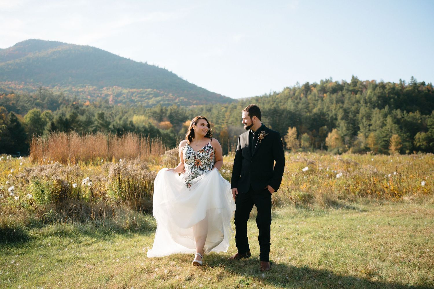Couple stands together in a scenic mountain meadow during an autumn wedding celebration.