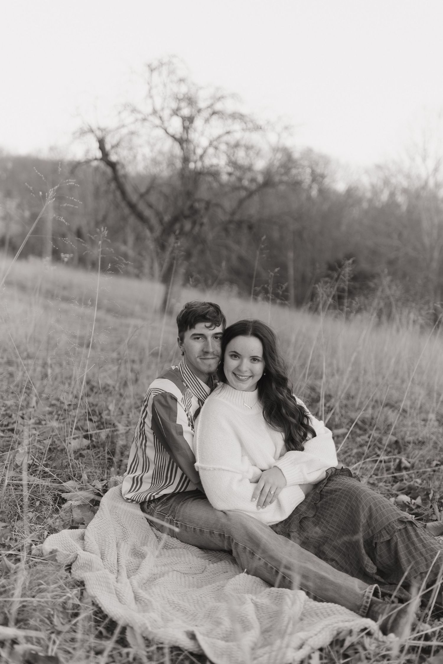A couple lounges together on a blanket in a rustic outdoor field setting in black and white.