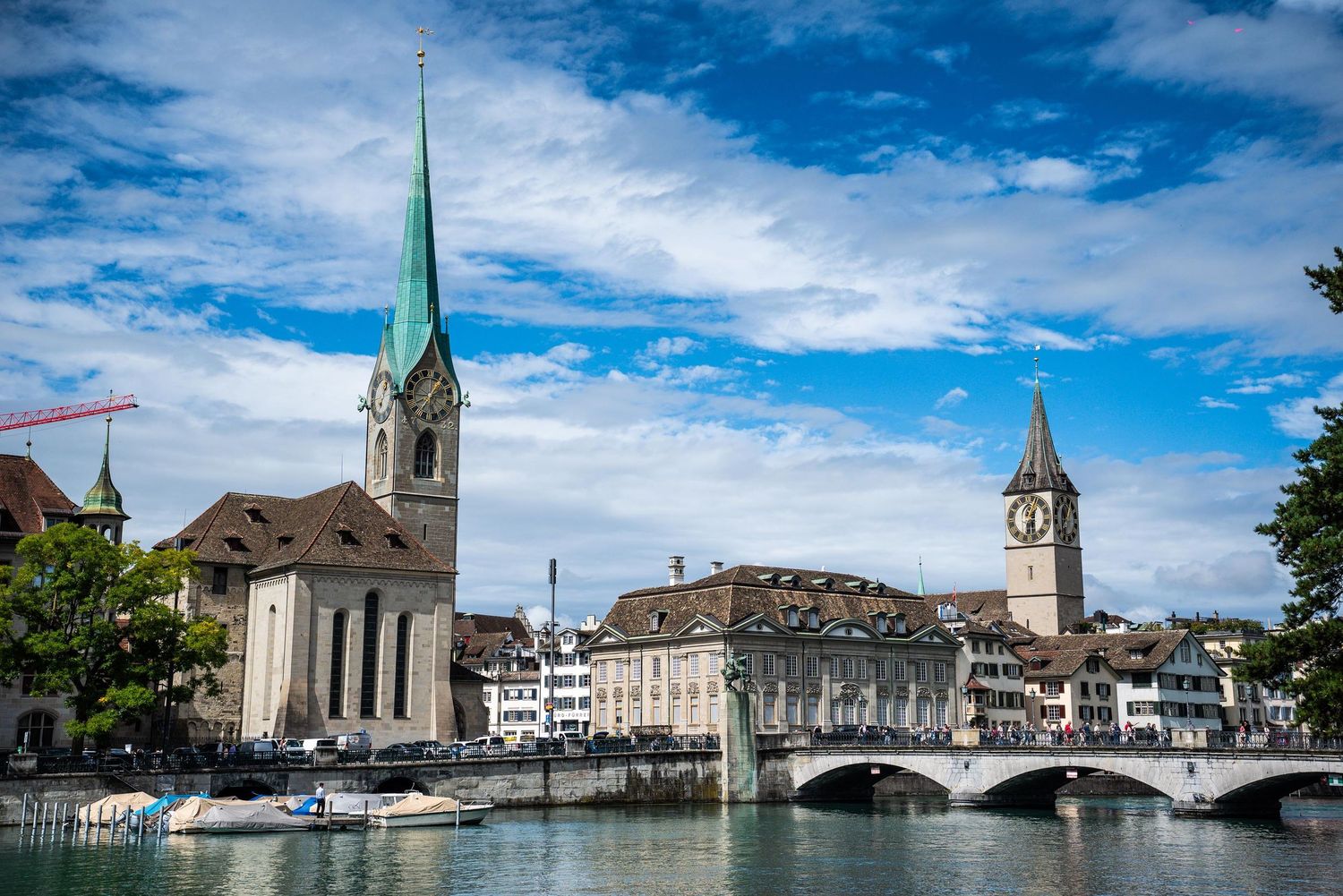 Panoramic view of Zurich's historic waterfront with church spires, bridges, and buildings along the Limmat River under blue skies.