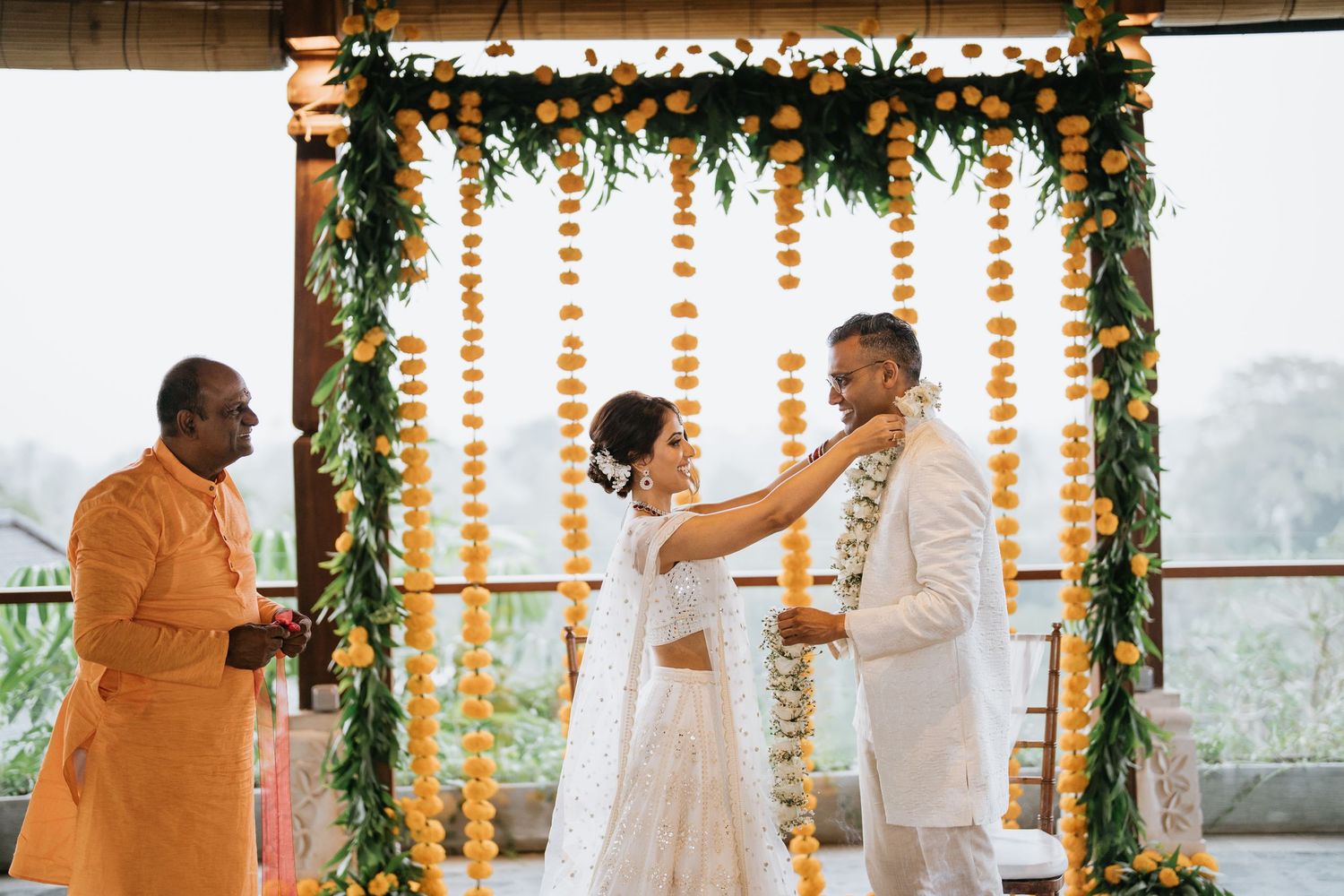Wedding ceremony setup with floral arch and white chairs against tropical beachfront backdrop.