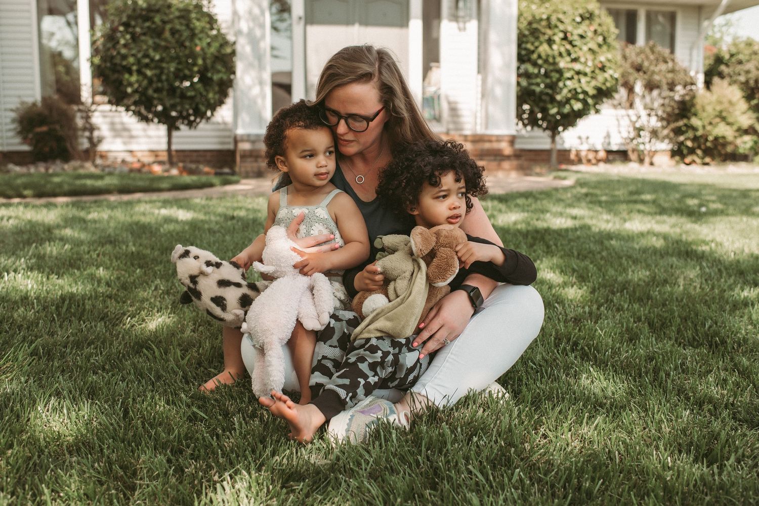 A loving family shares a tender moment together while sitting on lush green grass in front of their Virginia home.