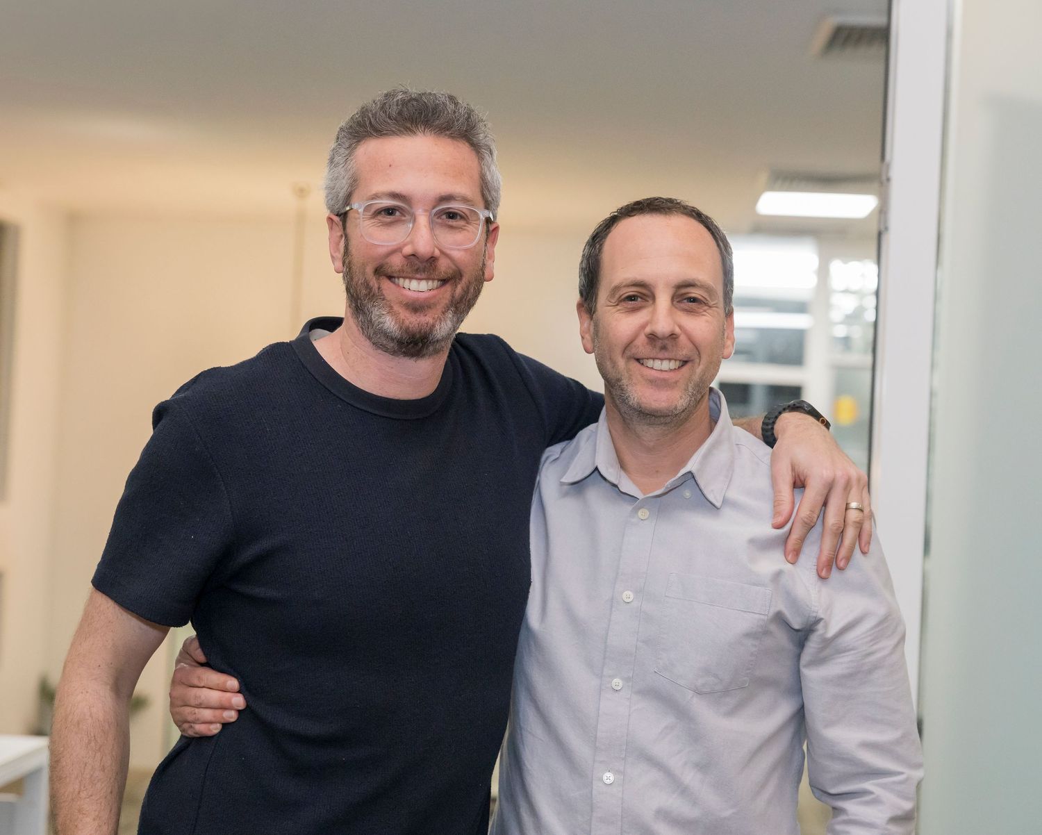 Professional colleagues in business attire stand together smiling for a photo in a modern office setting.