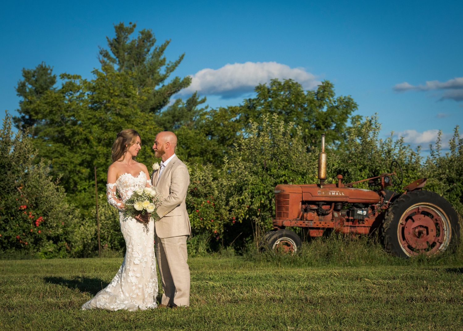 Newlyweds share an intimate moment by a brick garden wall at sunset.