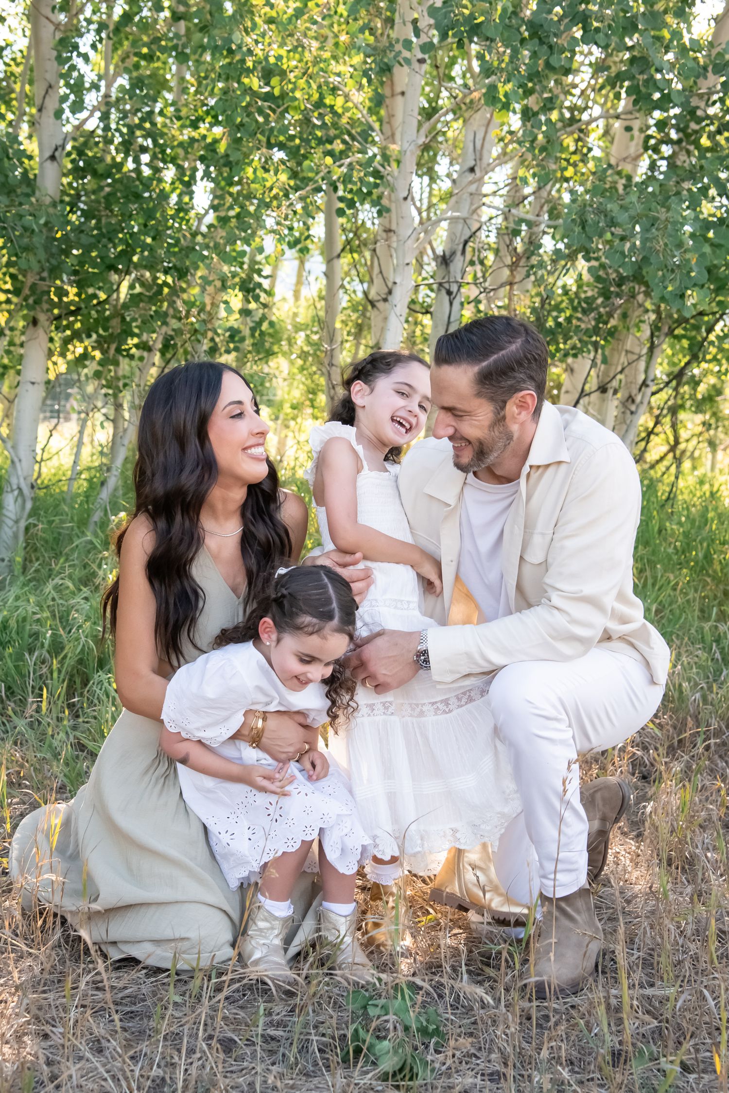 Family enjoying candid moments together while sitting in a sunlit aspen grove.