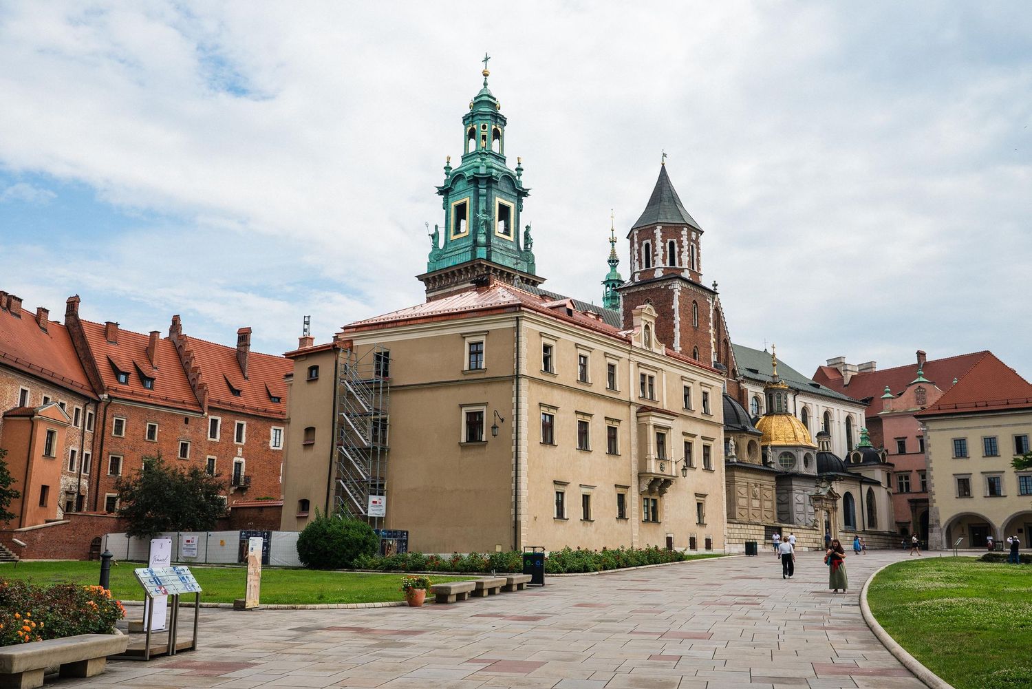 Historic Wawel Cathedral complex with green spire and towers stands along cobblestone path in Krakow, Poland.