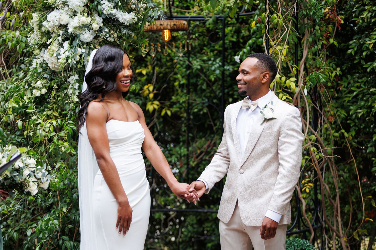 Wedding couple poses together in a lush garden setting with white flowers.