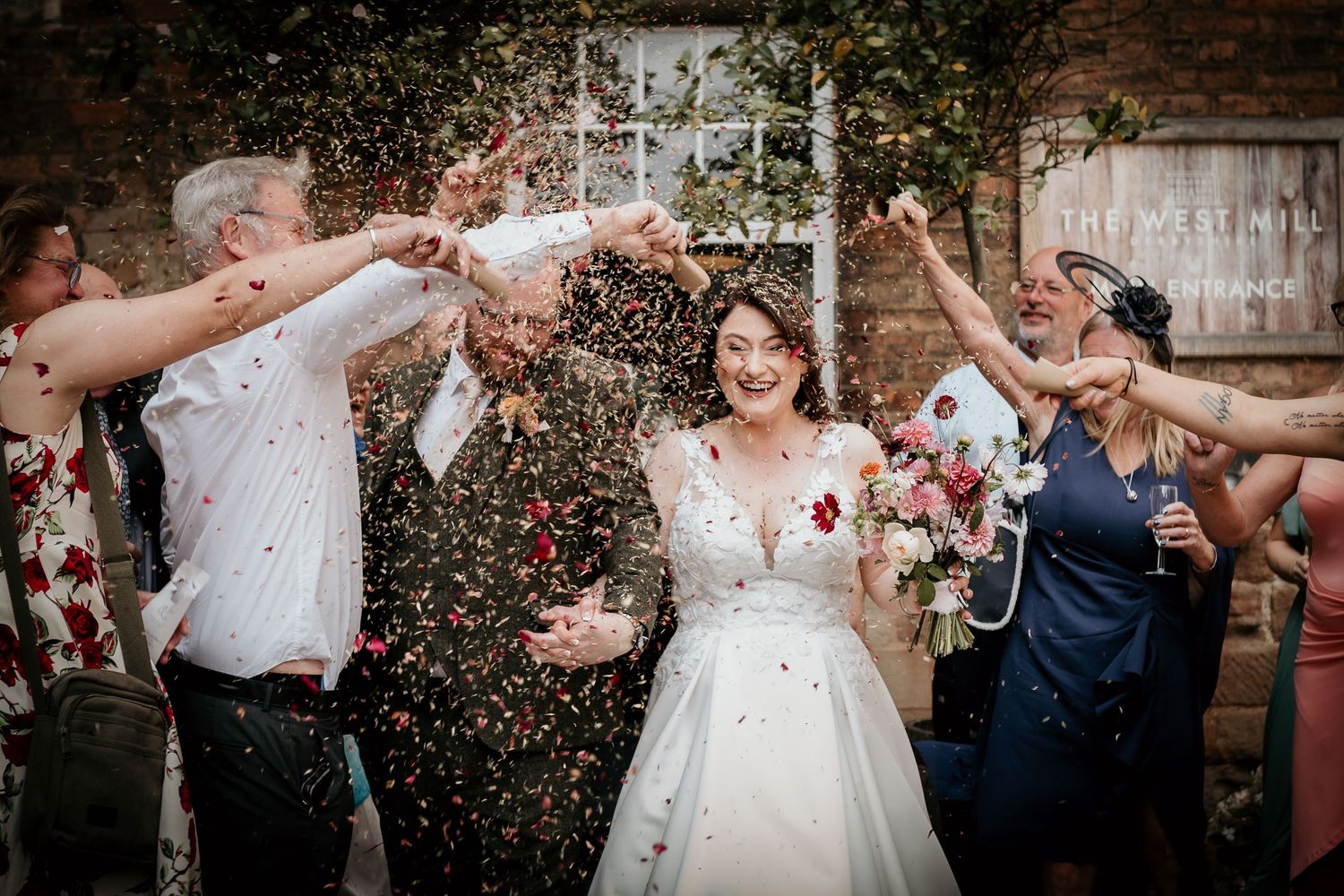 A joyful wedding celebration with guests throwing rice as the newlyweds walk outside a building in black and white.