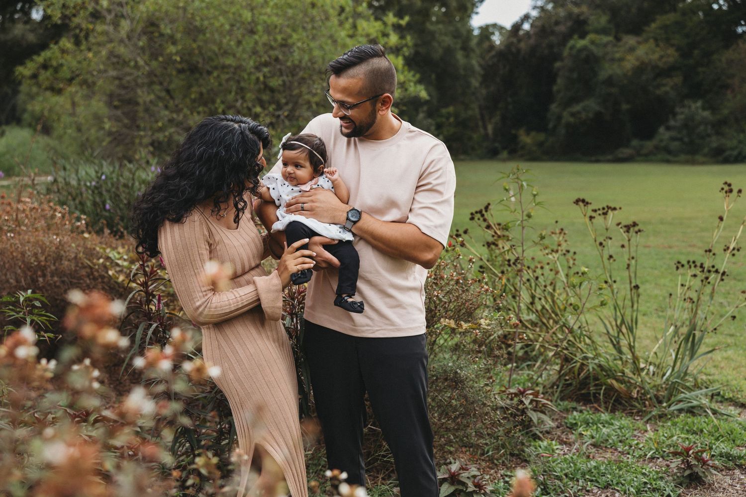 A family stands together in a sunlit grassy field during golden hour creating a warm and intimate outdoor portrait.