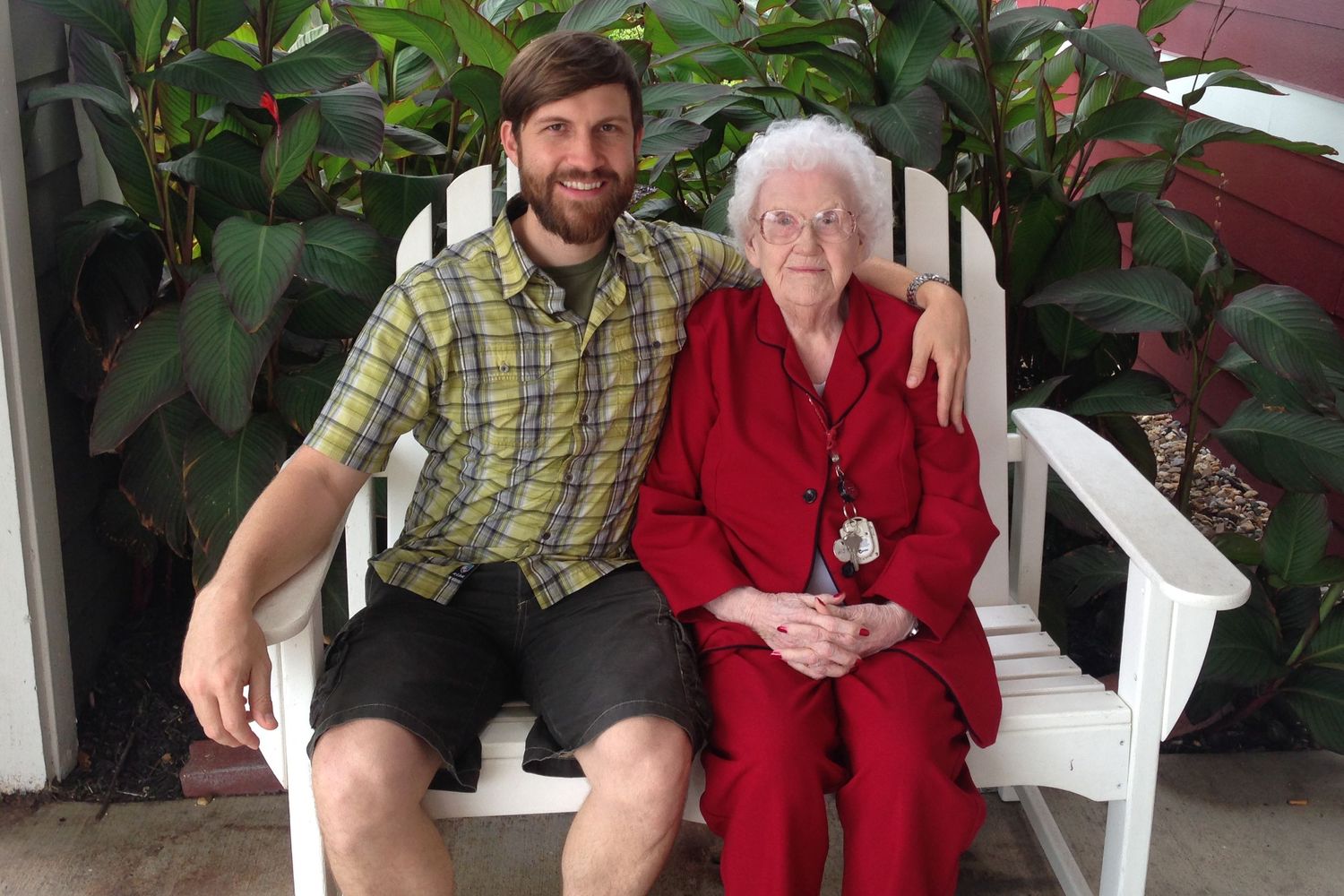 Grandson, Alex Kent and "Granny" Ena Maxine Kent sit next to each other outdoors with green plants behind.