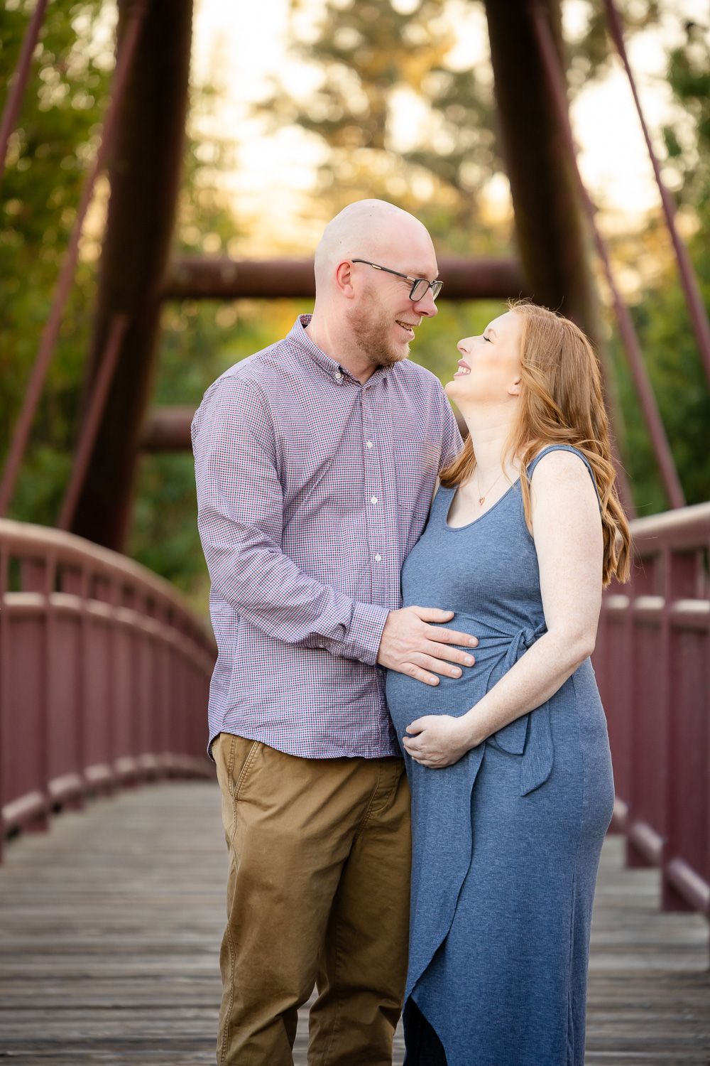 A couple stand on the red bridge at Vasona for their maternity photos during golden hour in Los Gatos, California with Bay Area photographer