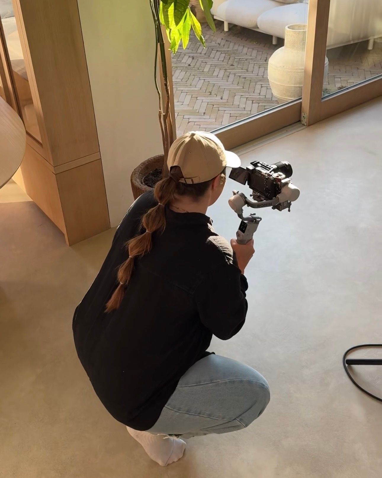 Photographer in black crouches with a vintage camera against white background.