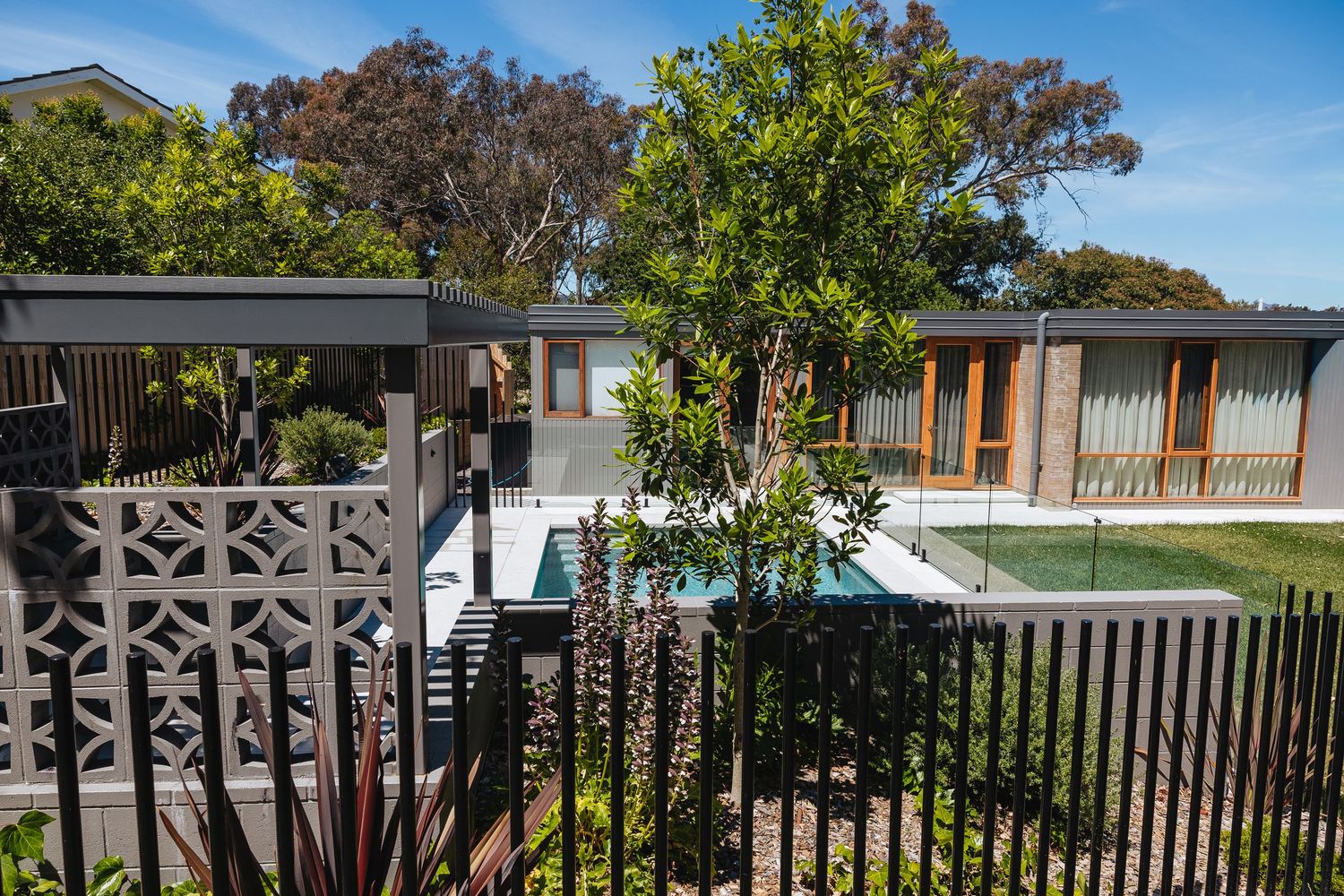 Black aluminum fence panels with decorative lattice pattern create an elegant boundary against lush green landscaping.