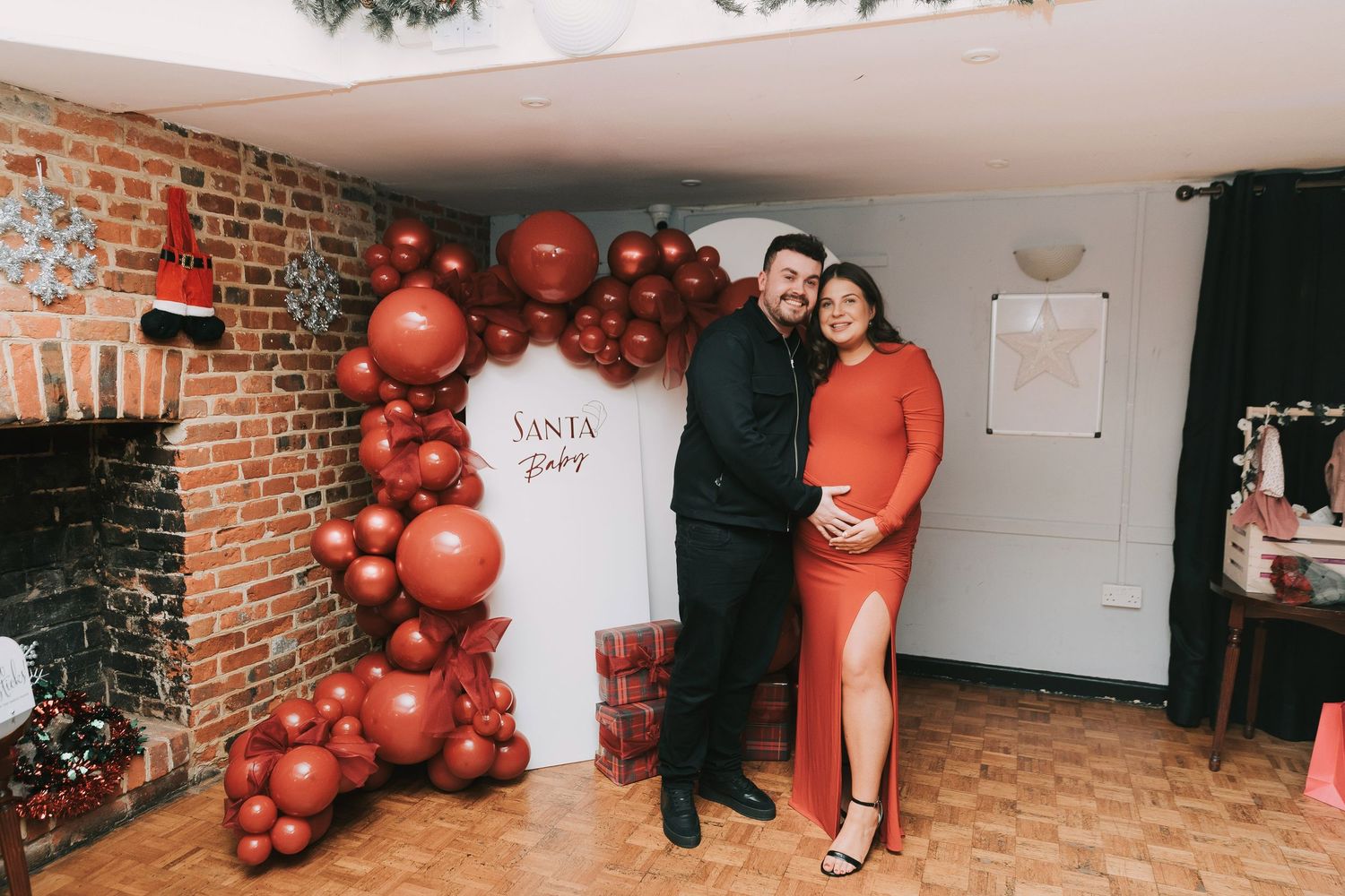 A festive balloon arch installation in progress with red balloons being arranged along a brick wall for expecting mum and dad to be.