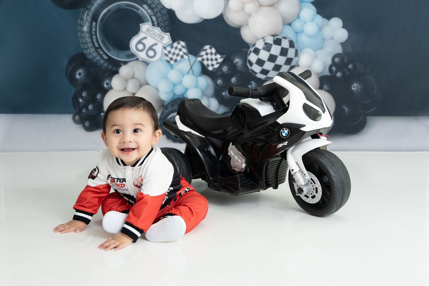 A decorative balloon arch in gray and blue tones with black and white motorcycle toys arranged beneath it.