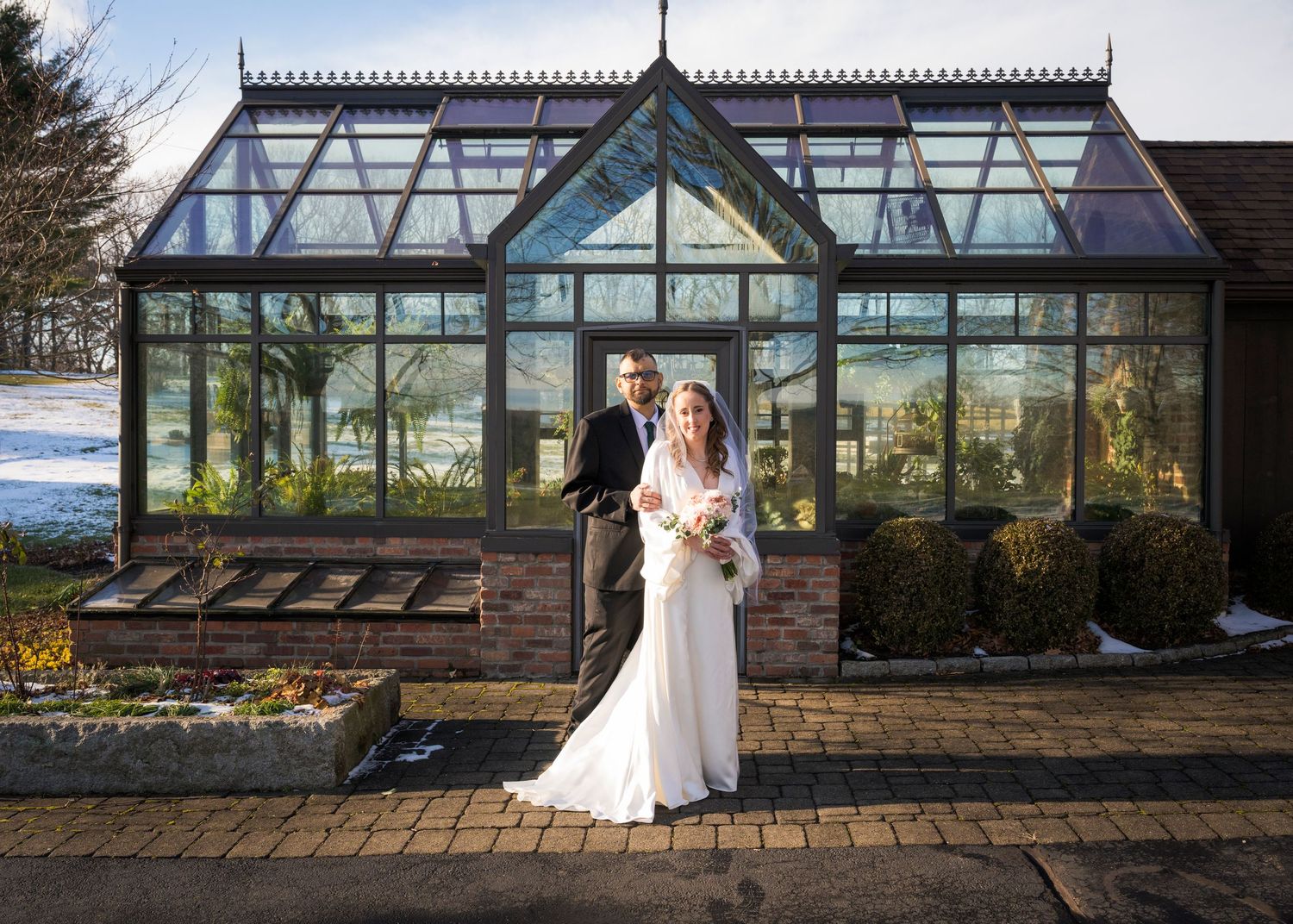 Newlyweds share an intimate moment outdoors with autumn foliage and rustic architecture in background.