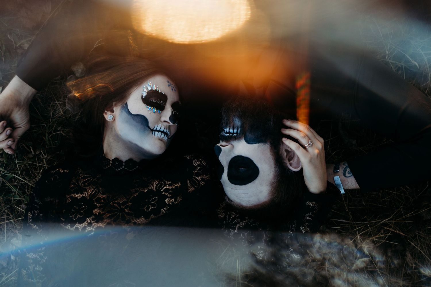 Two people wearing skull face paint lying on ground illuminated by warm orange light.