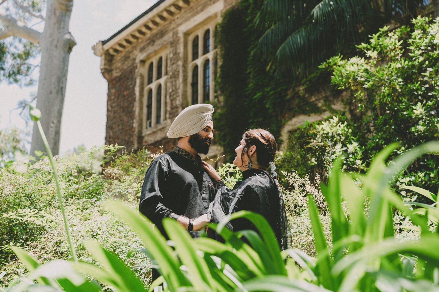 Person sits on a bench in a lush garden setting with stone architecture and dappled sunlight.