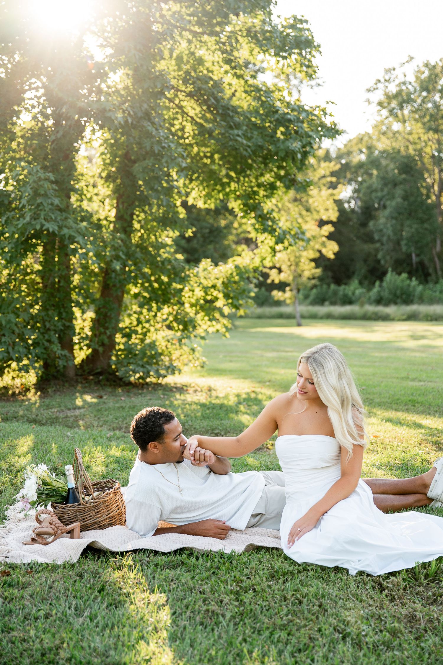 Romantic picnic scene on white blanket in sunlit grassy park.