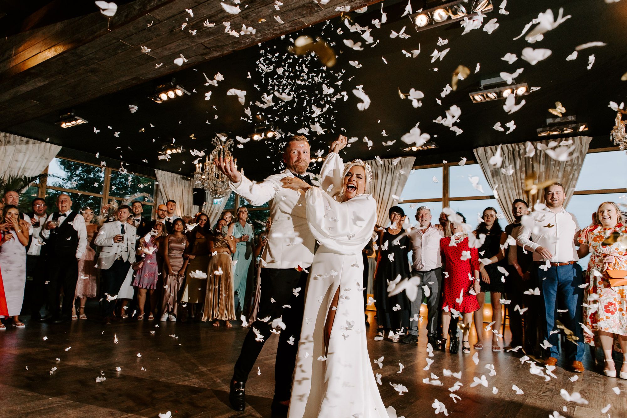 Wedding guests celebrate on dance floor as confetti falls during reception party celebration.
