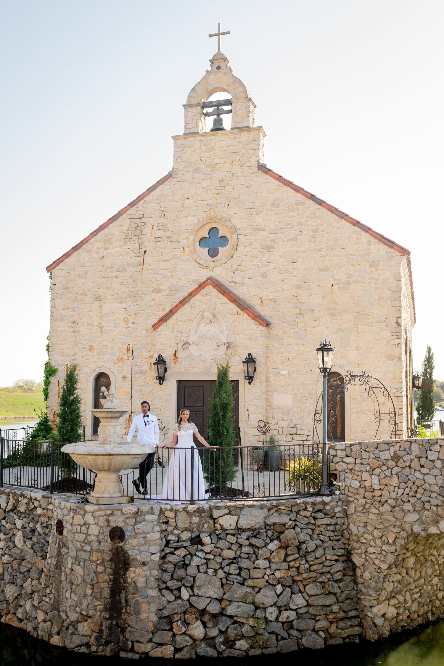 A stone church with cross and bell tower shown from multiple angles with stone wall in foreground.