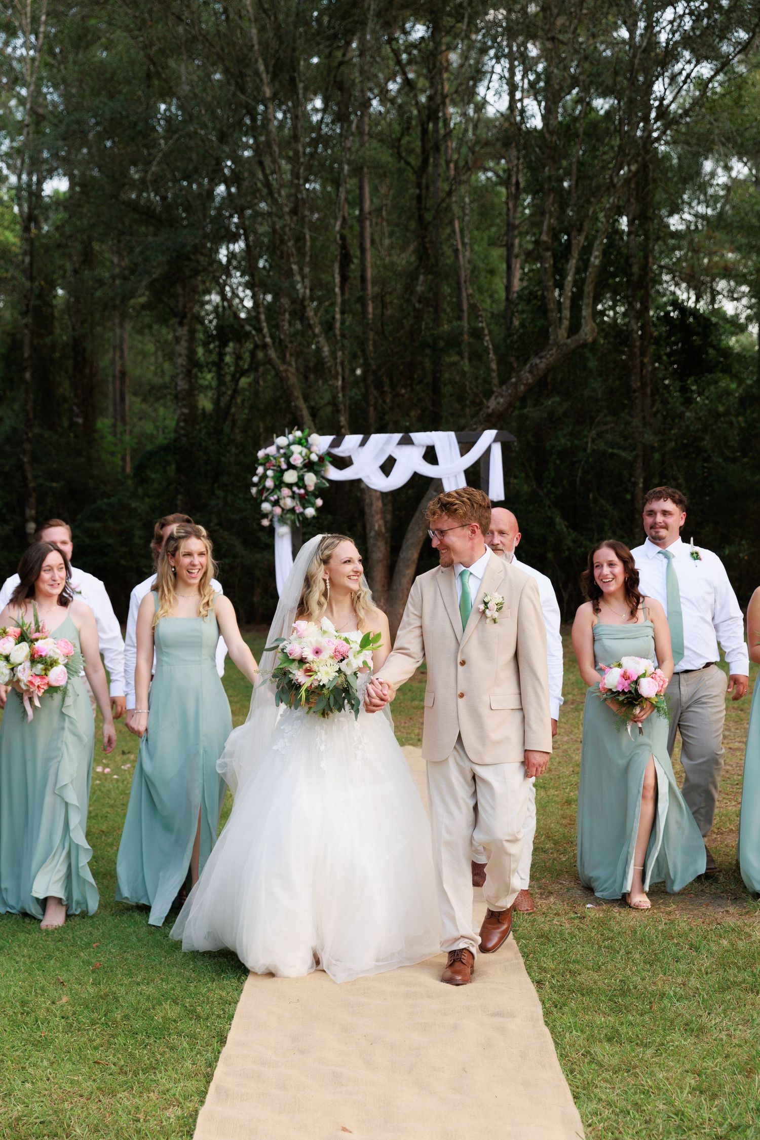 Newly married couple walking along brick path by white picket fence under tree canopy.