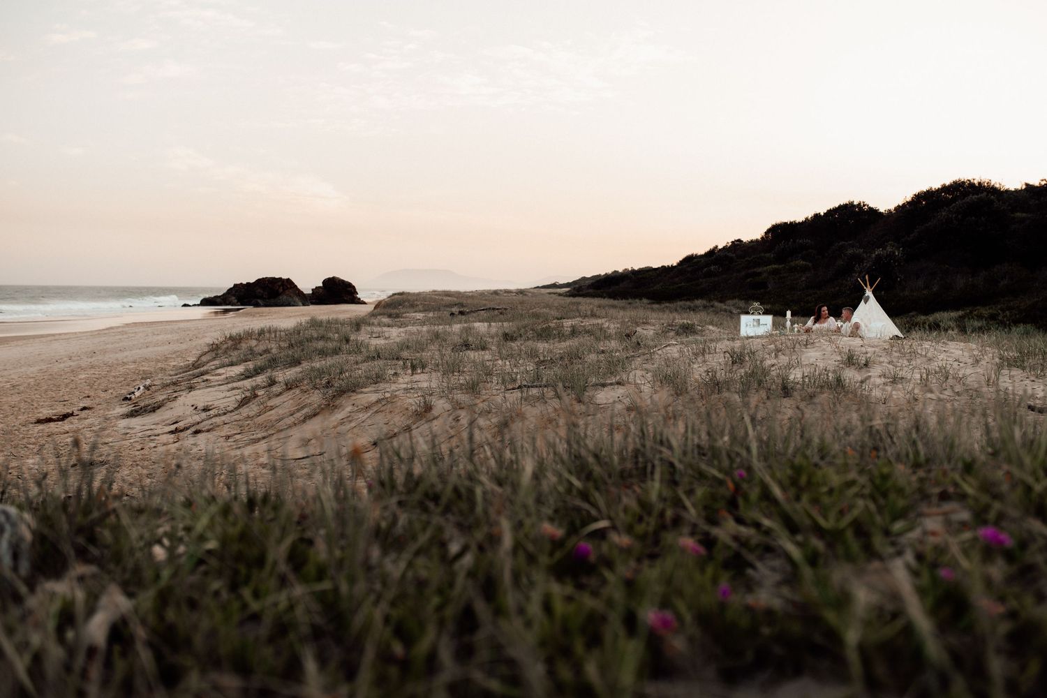 Scenic coastal landscape with a rustic camp tent overlooking a rugged beach at sunset along a misty shoreline.