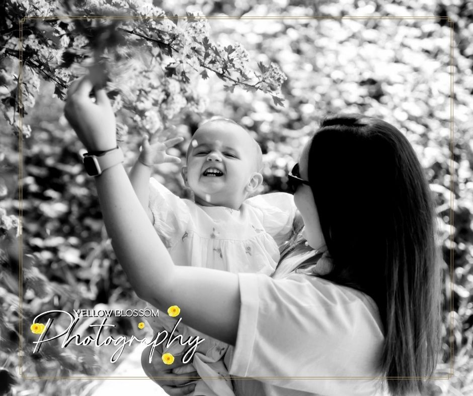 A joyful moment captured in black and white showing affectionate playtime with blossoming tree branches overhead.