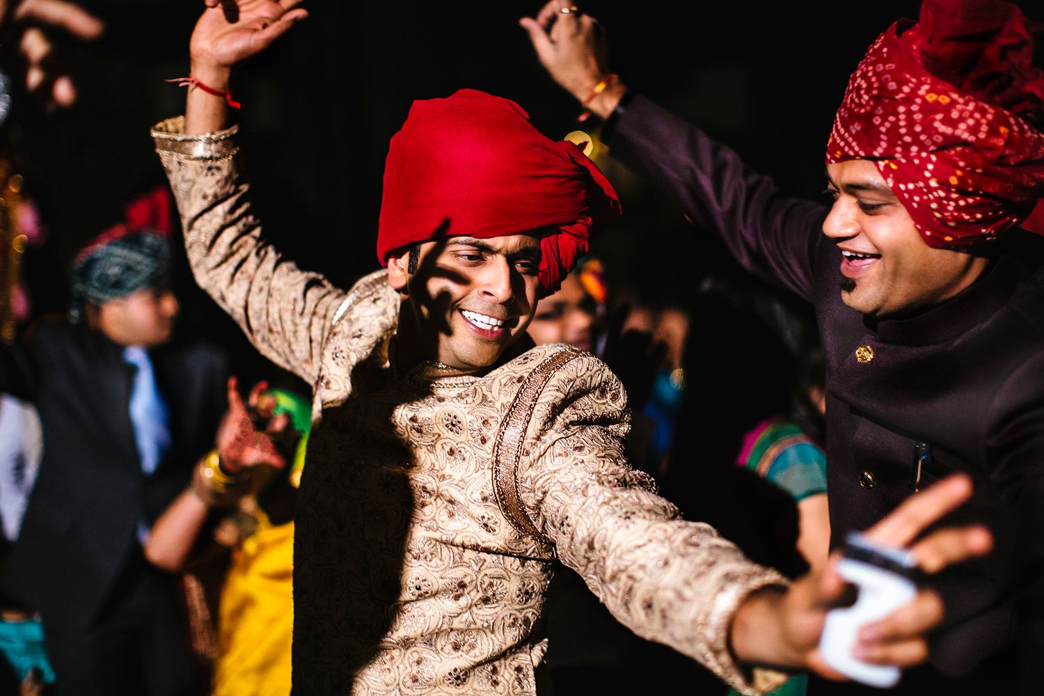 People dancing at a nighttime event wearing bandanas and warm clothing with arms raised in celebration.