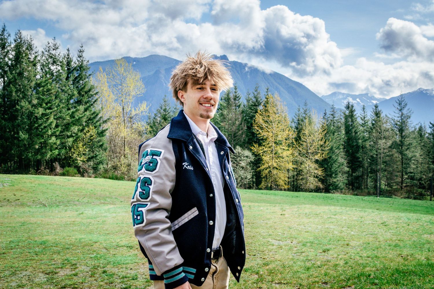 High school senior wearing letterman jacket during outdoor portrait session in Seattle with mountain views