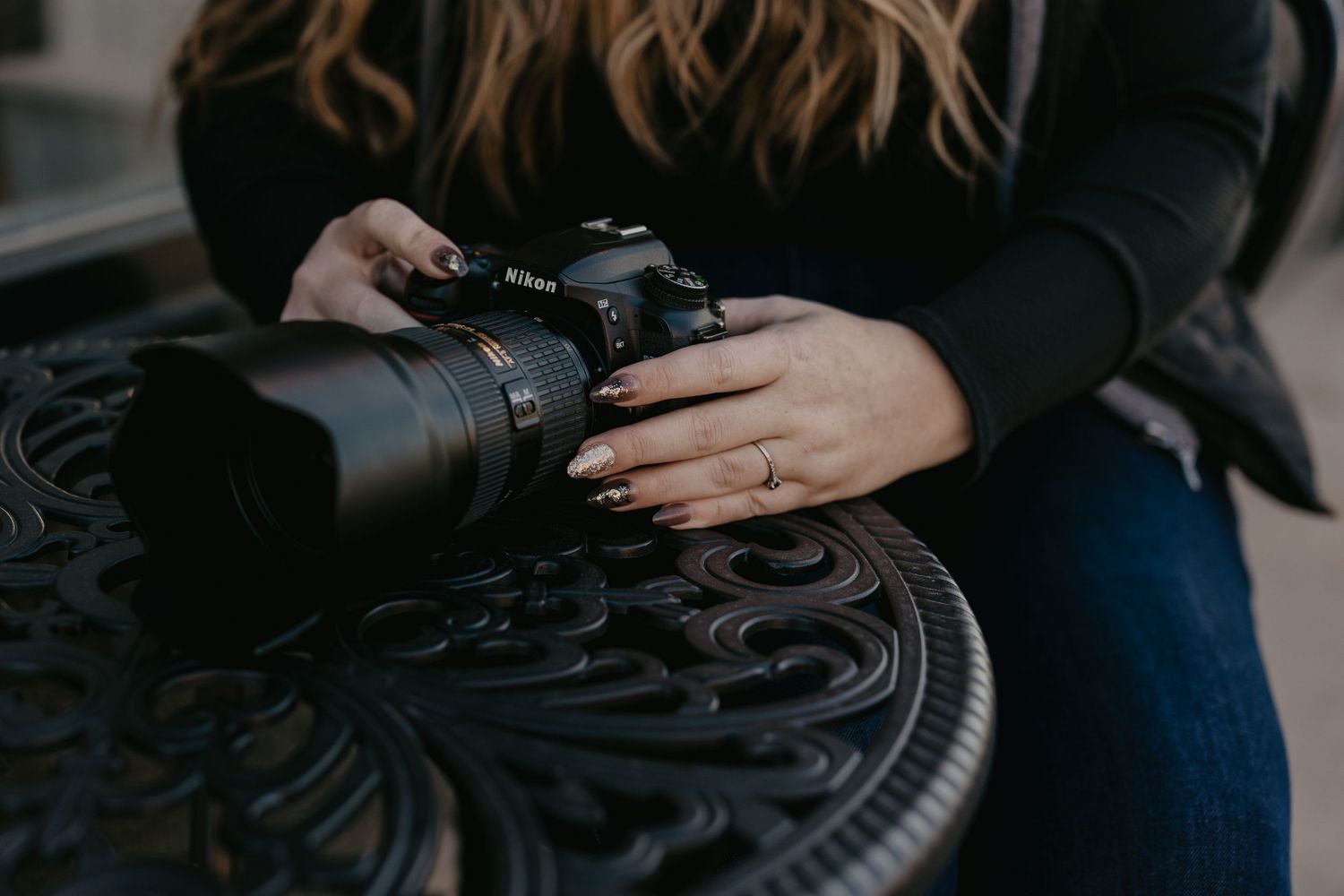 Woman holding a Nikon DSLR camera with large lens on ornate metal table.