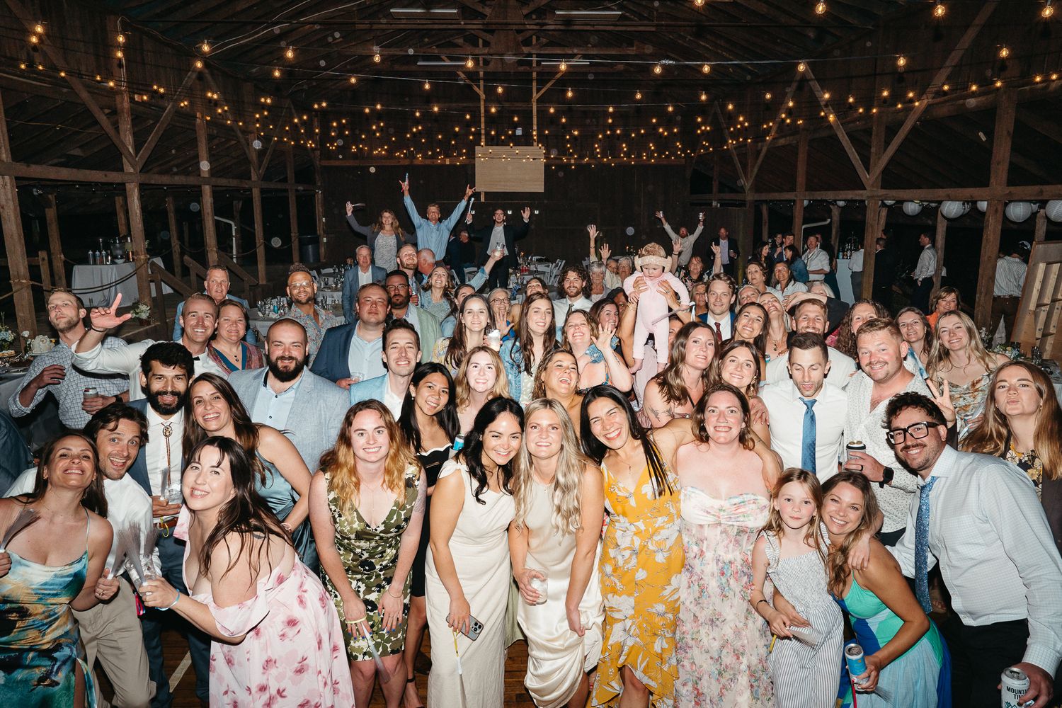 Wedding guests dancing and celebrating on a rustic dance floor under string lights at an evening reception. Asheville, NC Camp Venue