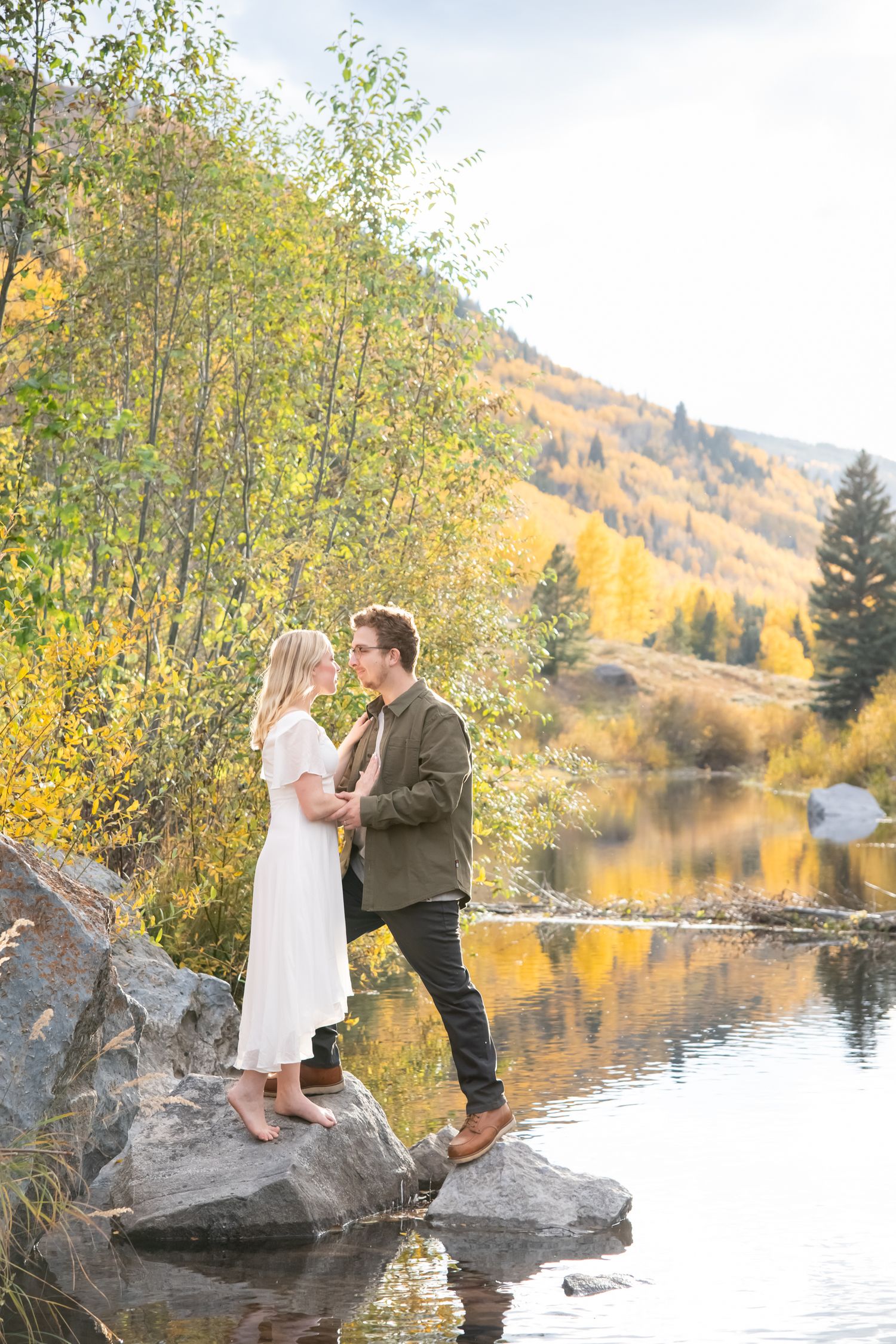 Couple sharing playful moments on rocks by a mountain lake during autumn.