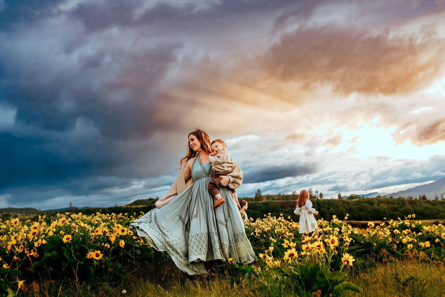Woman and child running through sunflower field under dramatic sunset sky.