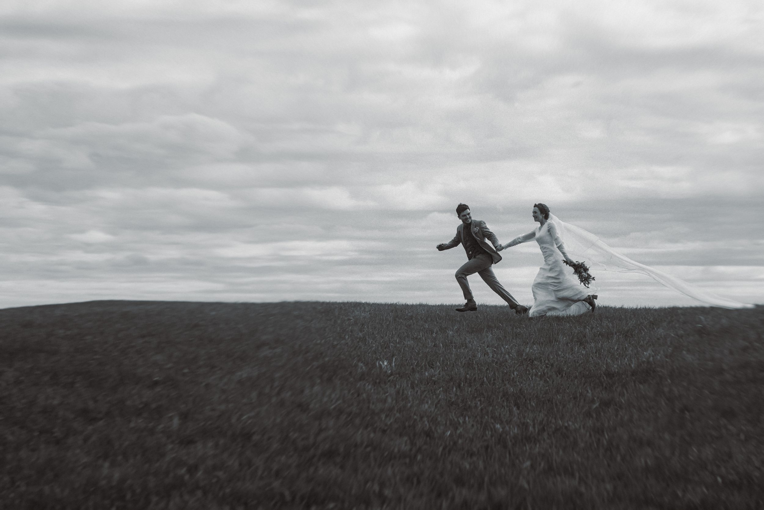 Silhouetted couple runs hand in hand across hilltop against cloudy sky.
