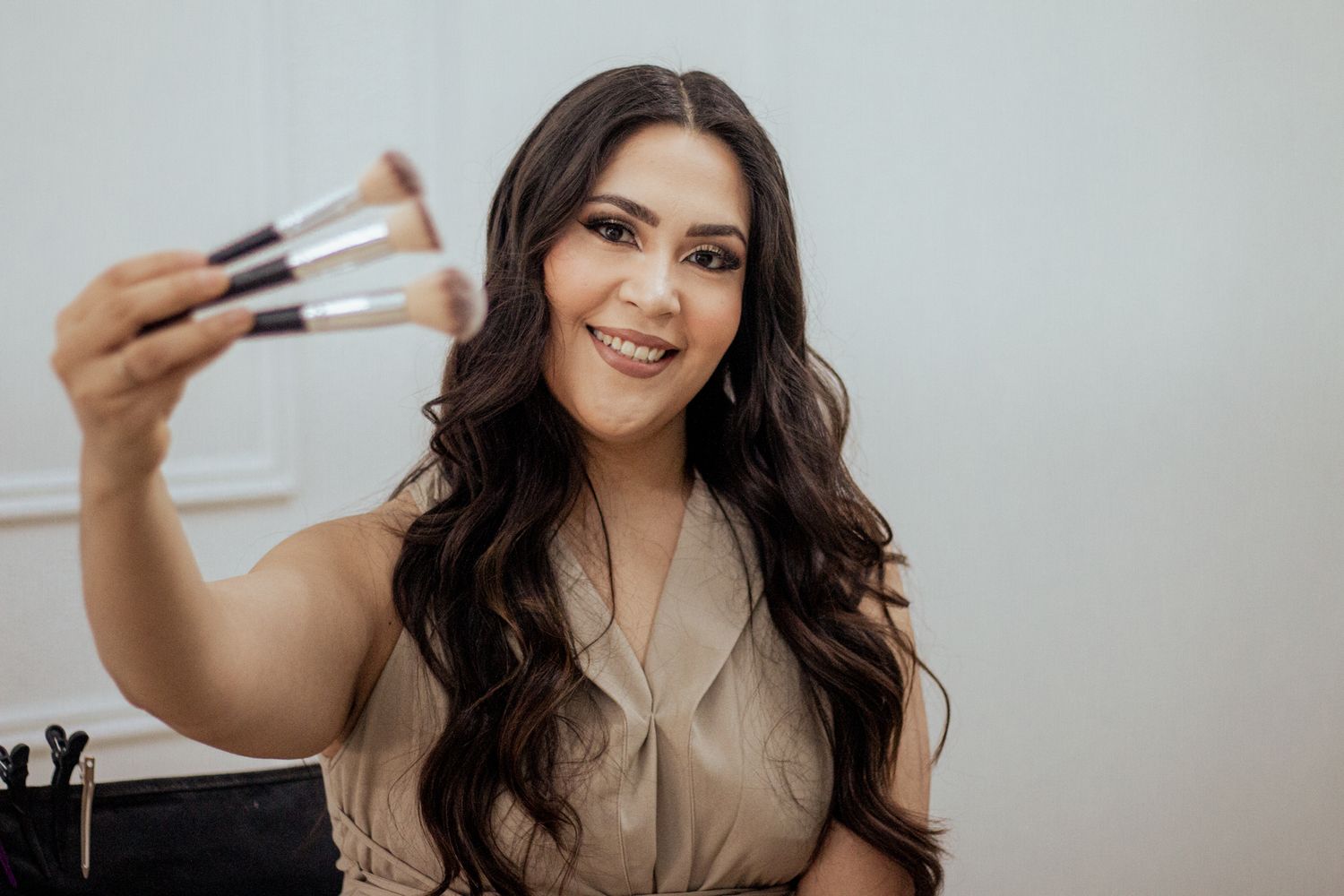 Beauty professional holding up makeup brushes against light gray background.