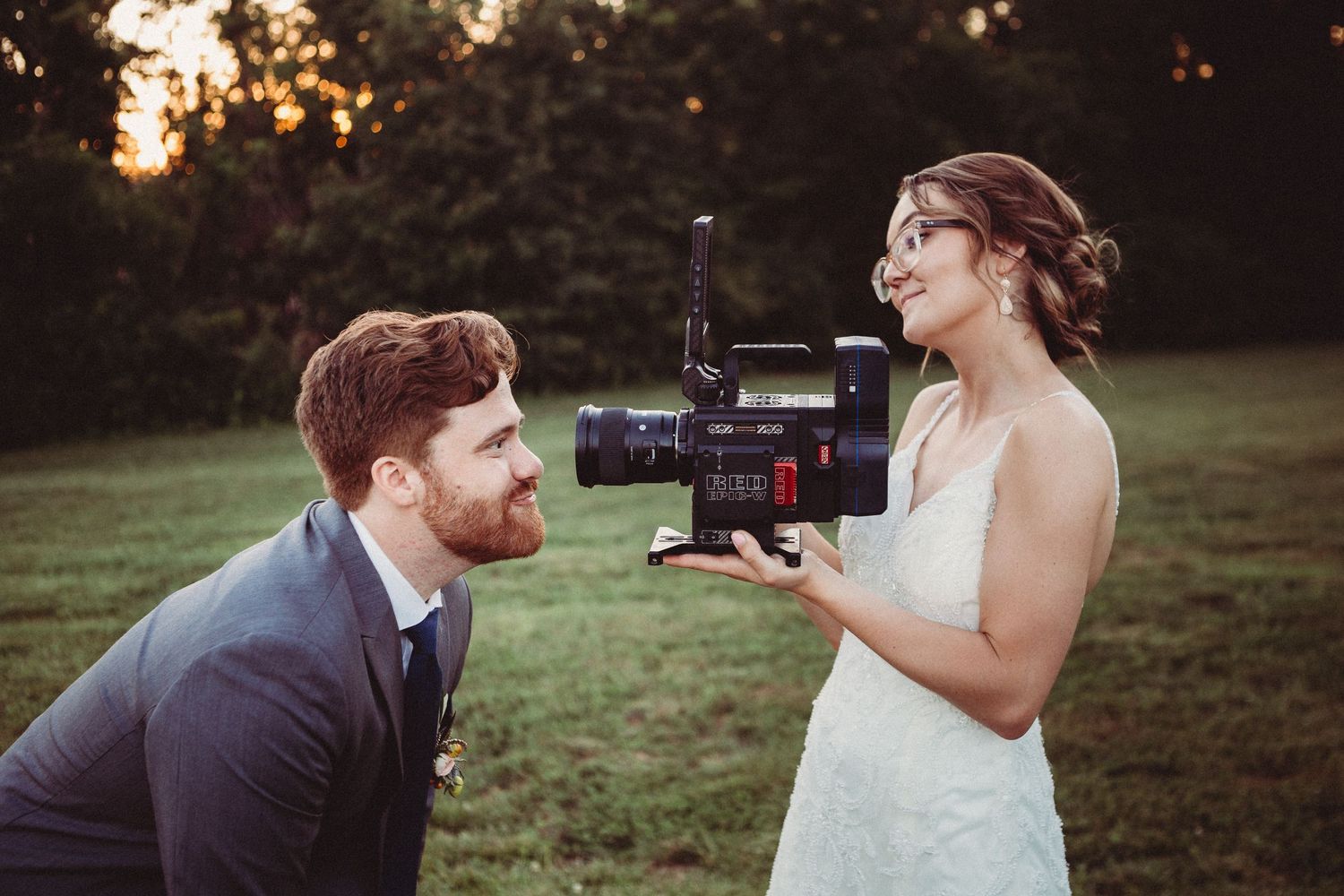 Creative wedding photography shot showing couple sharing playful moment with camera at sunset in outdoor setting. KC wedding Videographer.