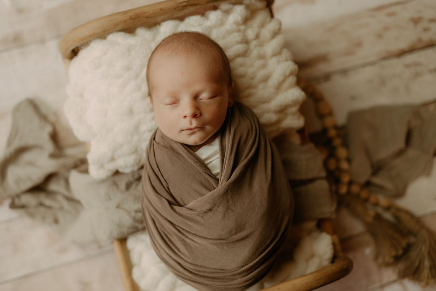 Peaceful sleeping newborn wrapped in soft brown fabric against textured backdrop.