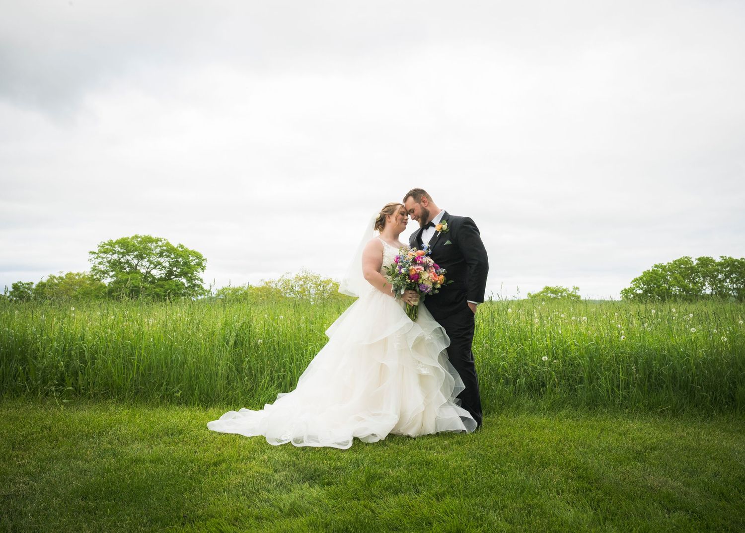 Newlyweds share an intimate moment outdoors with autumn foliage and rustic architecture in background.