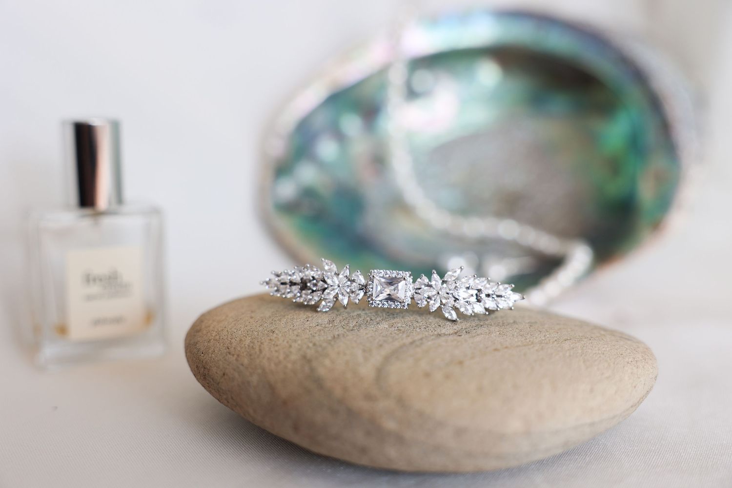 Sparkling diamond wedding ring displayed on a smooth stone with perfume bottle in background.