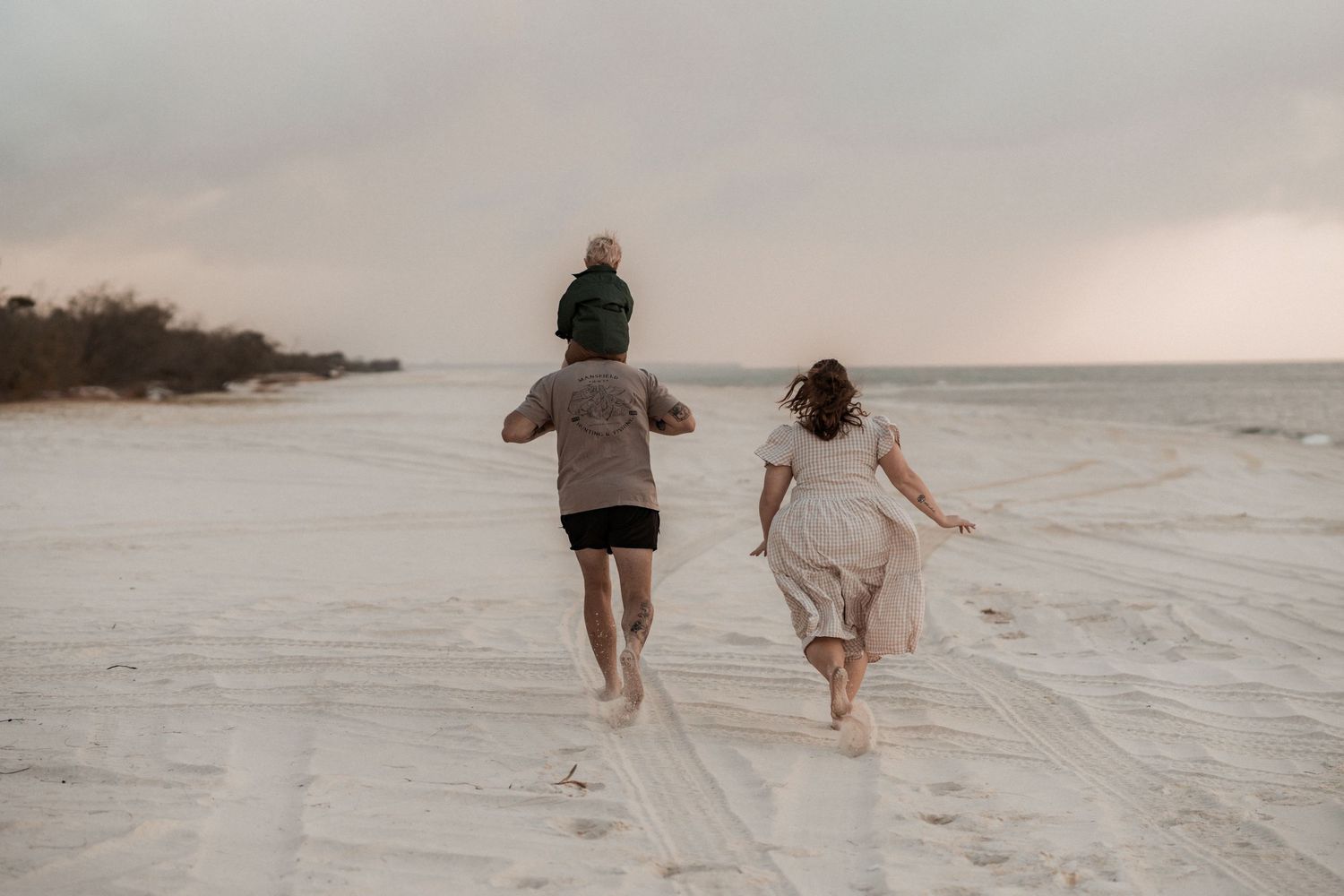 Two people walk together on a sandy beach during sunset with dramatic lighting creating silhouettes.