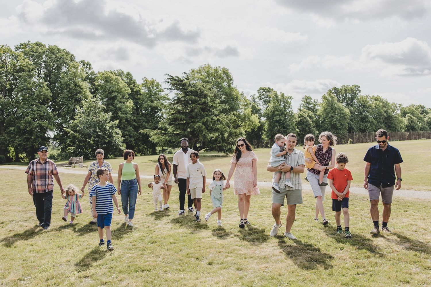 People walking together in a line across a sunny grassy field on a summer day.