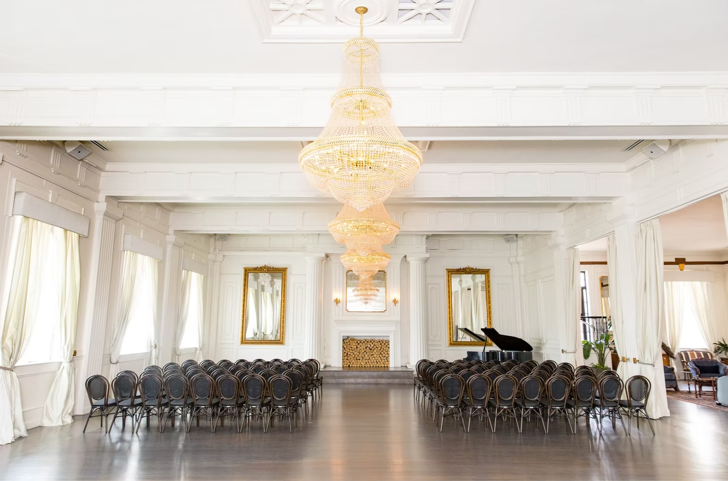 Elegant banquet hall with crystal chandeliers and rows of chairs arranged in a spacious white interior venue.