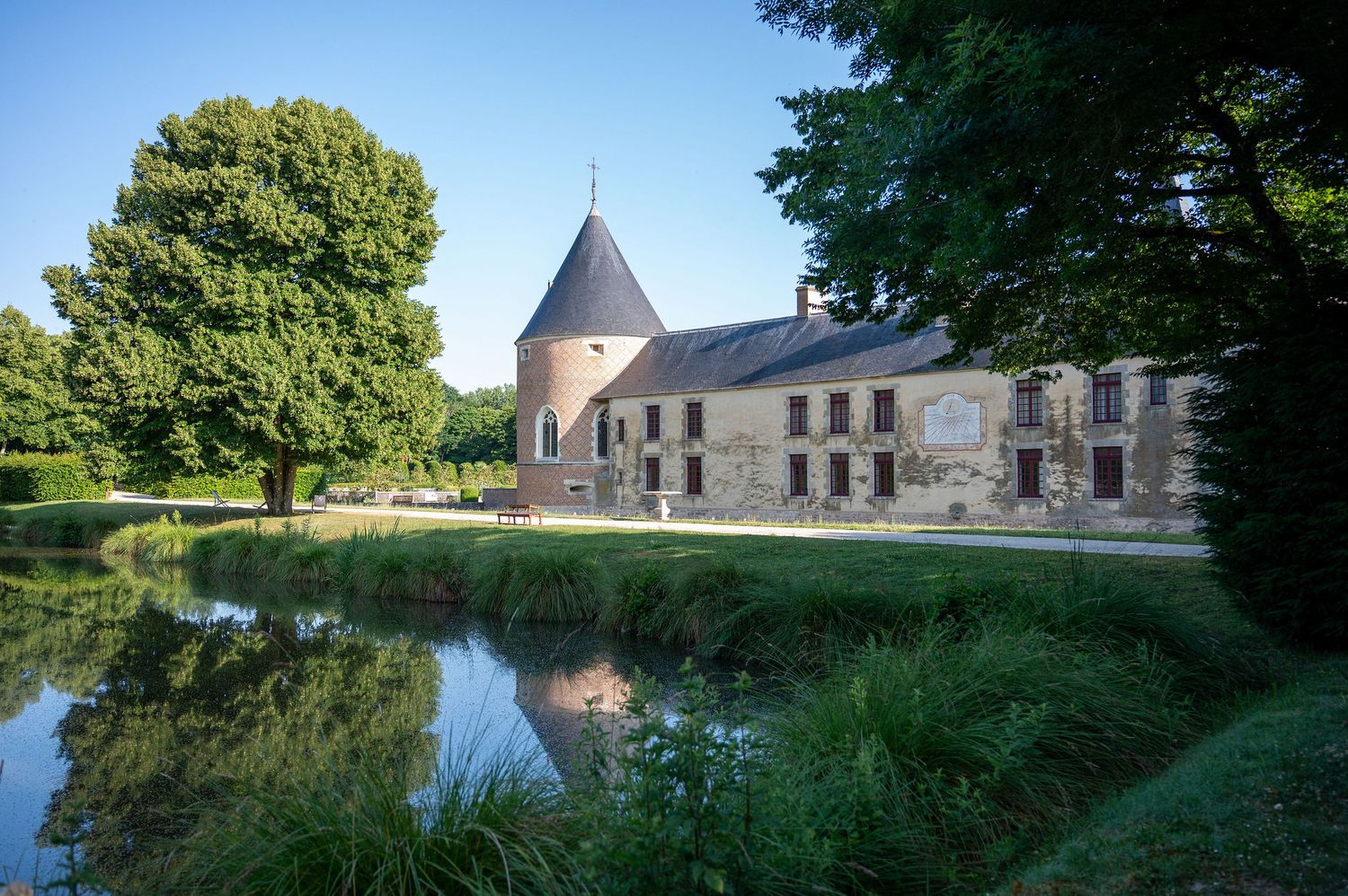 Une vue d’un château à l’architecture traditionnelle bordé d’un étang reflétant parfaitement les arbres et le bâtiment, illustrant l’ancrage