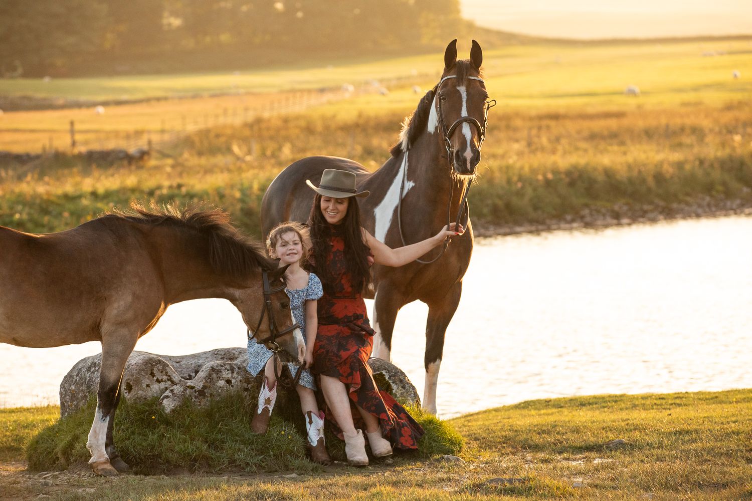 Horses and companions rest by a serene lake during golden hour.